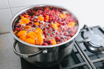 Fresh fruits are boiled in boiling water in a metal pan on the stove. Delicious stewed apricot, apples, cherries, raspberries. Photography, concept.