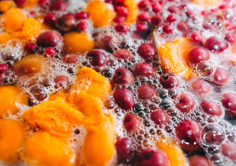 Fototapeta na wymiar Fresh fruits: apricots, cherries, raspberries, apples are boiled in boiling water in a metal pan on a stove with bubbles and foam close-up. Cooking delicious homemade compote. Photography, concept.