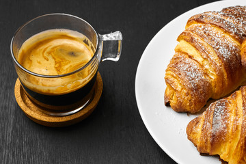 Cup of coffee and freshly baked croissants on a dark table. Served breakfast concept. French pastry...