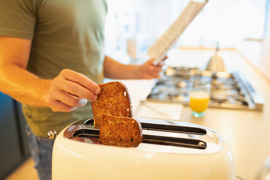 Close up man making toast and reading newspaper in morning kitchen