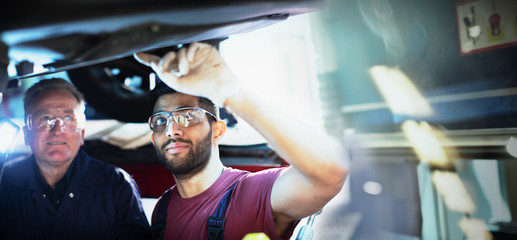 Male mechanics working under car in auto repair shop