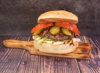 Tasty beef burger with lettuce, tomatoes, pickles, and sauce, on a wooden board