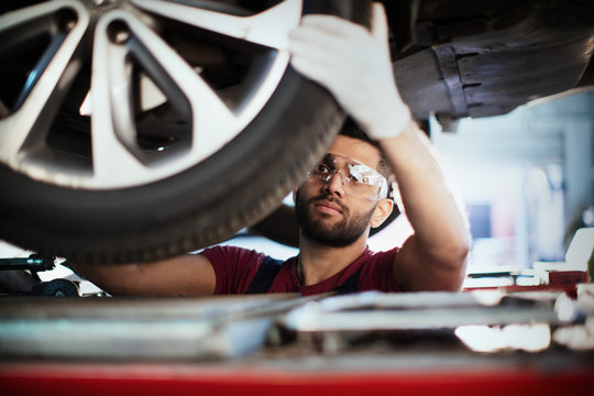 Male mechanic working under car, examining tire in auto repair shop