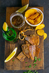 Dried cod with pepper with beer, lemon and potato chips on dark wooden board. Snack on fish with...