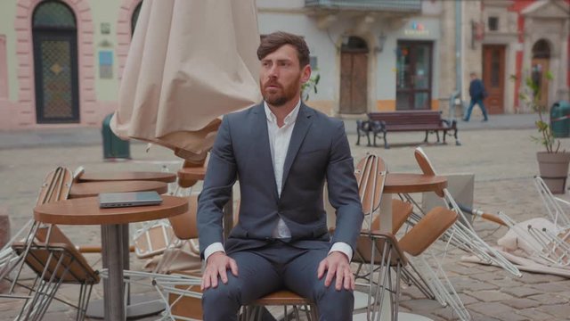 Depressed bearded restaurateur in suit lost his business sitting outdoors empty terrace of closed restaurant city center. Crisis 2020. Global unemployment. Commercial apocalypse.