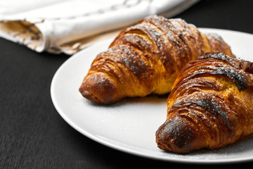 Freshly baked plain croissants on a white plate near serviette on a black wooden background. Homemade french pastry.