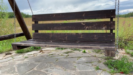 Big vacant wooden swing in a countrysyde in summer, green grass lawn on background, nostalgia and...