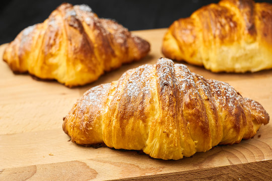 Close up three freshly baked croissants with sugar powder on a wooden desk. Puff french pastry. 