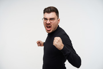 Studio photo of young disgruntled short haired unshaved guy raising his fists while being ready to...