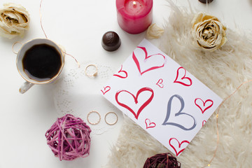 Coffee, sweets, candle, gold rings, red dry rose and heart card decoration, placed on white concrete bac