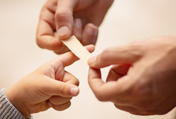 Dad putting a plater band-aid on his sons finger on white background, close-up, hands only