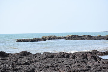 Fototapeta na wymiar Black rocks in the seashore.A view from Goa beach.