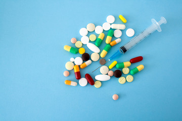 Multi-colored pills and capsules placed on a blue-green background with a syringe in the center of the conceptual image, isolated