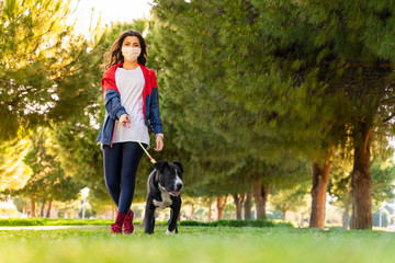 woman wearing a protective mask is walking alone with a dog outdoors because of the corona virus pandemic covid-19