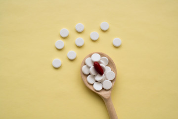 round white tablets with one red capsule on a wooden spoon on a yellow background, tablets are scattered in the center from bottom to top, isolated.