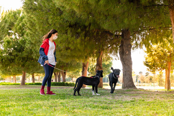 woman wearing a protective mask is walking alone with a dog outdoors because of the corona virus pandemic covid-19