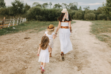 Mom with 2 daughters walks the village in white dresses on a summer day, life on the farm