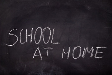 The inscription school at home on the school blackboard. White letters on a black background in the classroom. Dark background.