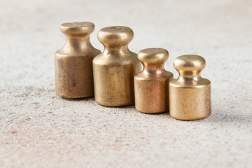 Four antique bronze weights for scales on concrete background.