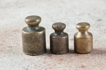 Three antique bronze weights for scales on concrete background.