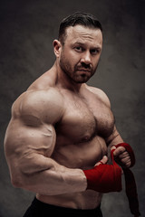 Fototapeta na wymiar Sportive adult male wearing sportswear showing biceps, looking at the camera in a dark studio