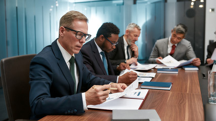 Concentrated business people in formal wear analyzing sales report while having a meeting in the office