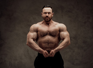 Fototapeta na wymiar Shirtless adult male bodybuilder doing a muscle showing with a serious face in a studio