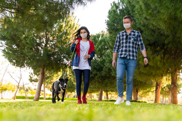 Naklejka na ściany i meble young couple wearing a protective mask is walking alone with a dog outdoors because of the corona virus pandemic covid-19