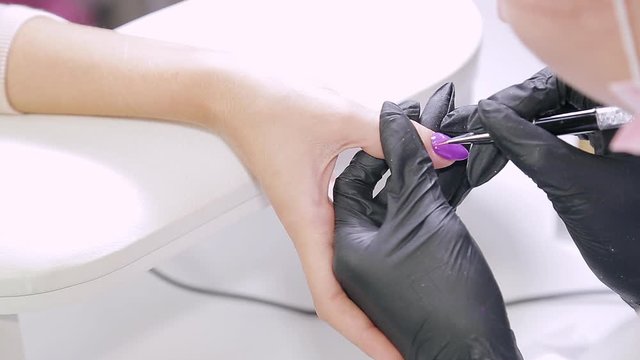Woman manicurist in a beauty salon applies a matte coating on gel polish.
