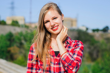 young blonde girl in a red shirt on the roof of the building looks at the camera