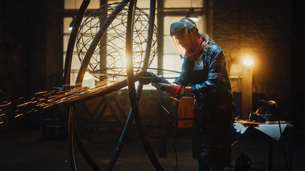 Shot of Talented Innovative Female Artist Using an Angle Grinder to Make Abstract, Brutal and Expressive Metal Sculpture in a Workshop. Contemporary Fabricator Creating Modern Steel Art.