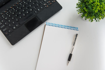 Top view mockup of laptop, green plant, pen and notebook on white background. Planning layout concept with copy space