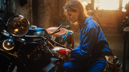 Young Beautiful Female Mechanic is Working on a Custom Bobber Motorcycle. Talented Girl Wearing a...
