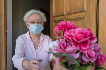 Senior woman with face mask gets flowers at the house door