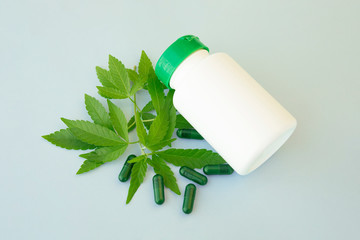 Cannabis leaves with green capsules pill and white bottle. Alternative medicine, Medical hemp concept