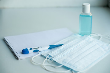 Fototapeta premium on a white table are a Notepad and protective equipment for the epidemic - medical masks, a thermometer and hand sanitizer