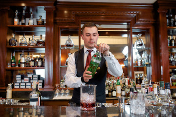 In alcohol we trust. Young bartender standing at counter and pouring alcohol to prepare iced cocktail in the bar