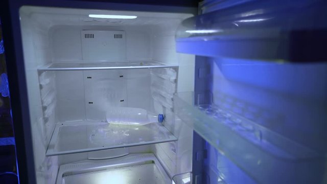 Lack of money due to the financial crisis. A fired man suffers from depression and insomnia. A crisis. The guy puts milk into the empty fridge. Night hunger. Hangover. Bachelor's fridge. Empty fridge.