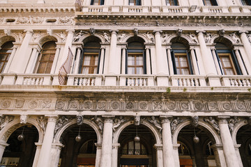 Fototapeta na wymiar Building Fondazione Musei Civici di Venezia in Venice, Italy. Stone bas-reliefs on the facade of building in Piazza San Marco, classic Venetian windows, columns, balconies with small columns, stucco.