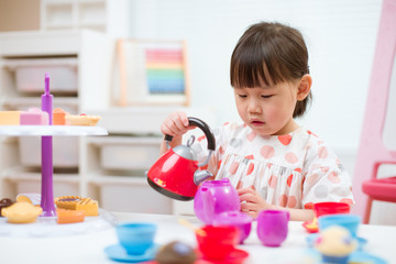 Obraz na płótnie Canvas toddler girl prerend play preparing tea party at home