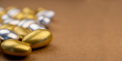 Side view and shallow depth of field of silver and gold almond candies for special events. Luxury sweet confections with textured background and copy space