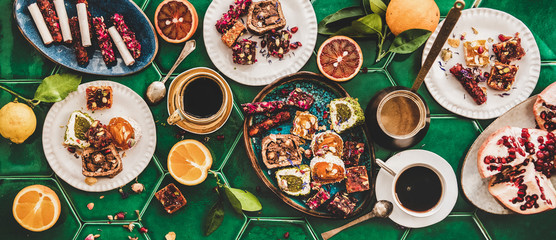 Flat-lay of variety of Turkish traditional lokum sweet delight with Turkish coffee in cups and fresh fruits over green Moroccan tile table, top view. Middle East typical dessert food