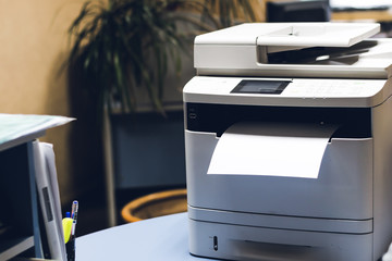 A large printer prints a white sheet with space for text in the office. blank paper in the workplace.