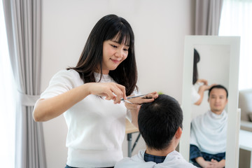 Obraz na płótnie Canvas Asian young man with her girlfriend hairdresser cutting hair with Haircutting scissors at home they stay at home during time of home isolation against Novel coronavirus or COVID-19