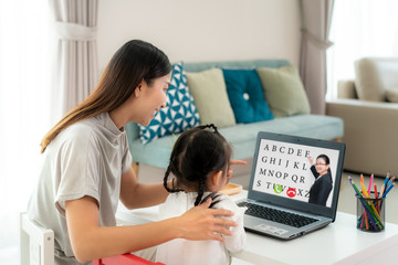 Asian kindergarten school girl with mother video conference e-learning with teacher on laptop in...