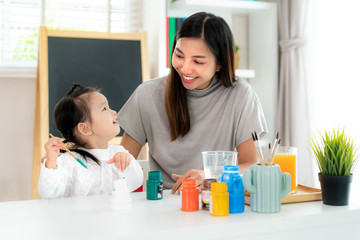 Asian kindergarten schoolgirl with mother painting Plaster doll with Acrylic water color paint in living room at home. Homeschooling and distance learning..