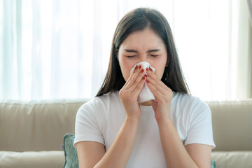 Asian woman sick and sad with sneezing on nose and cold cough on tissue paper because influenza and...