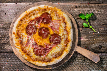Homemade Italian pepperoni pizza topped with ham and basil on a old wooden board