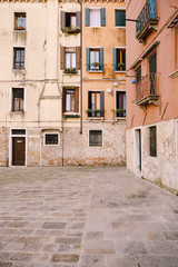 Fototapeta na wymiar Close-ups of building facades in Venice, Italy. Ancient street, facades of peach and yellow buildings. Windows with wooden blue shutters. Stone paving tile