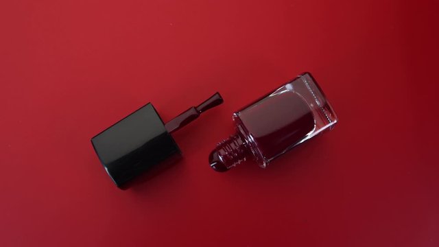 Bottle of nail polish lies on red background. Red nail polish drips onto red surface. Concept. Master of manicure.